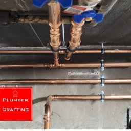 Miedziane rury instalacji wodnej zamocowane do sufitu i ściany, z zaworami kulowymi. Widoczne łączenia i uchwyty mocujące. Ujęcie od dołu.