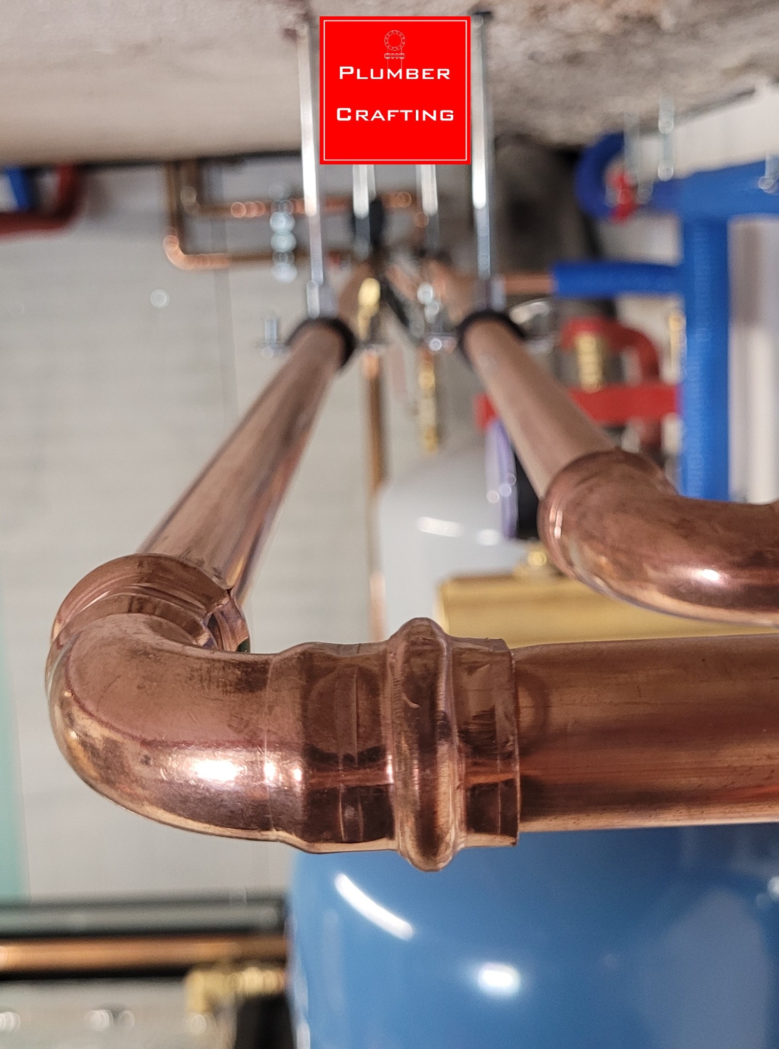 Miedziane rury instalacji hydraulicznej z precyzyjnymi złączami, zamontowane pod sufitem, z widocznym zbiornikiem wyrównawczym i elementami mocującymi.