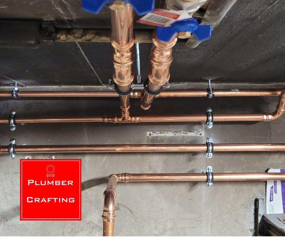 Miedziane rury instalacji wodnej zamocowane do sufitu i ściany, z zaworami kulowymi. Widoczne łączenia i uchwyty mocujące. Ujęcie od dołu.