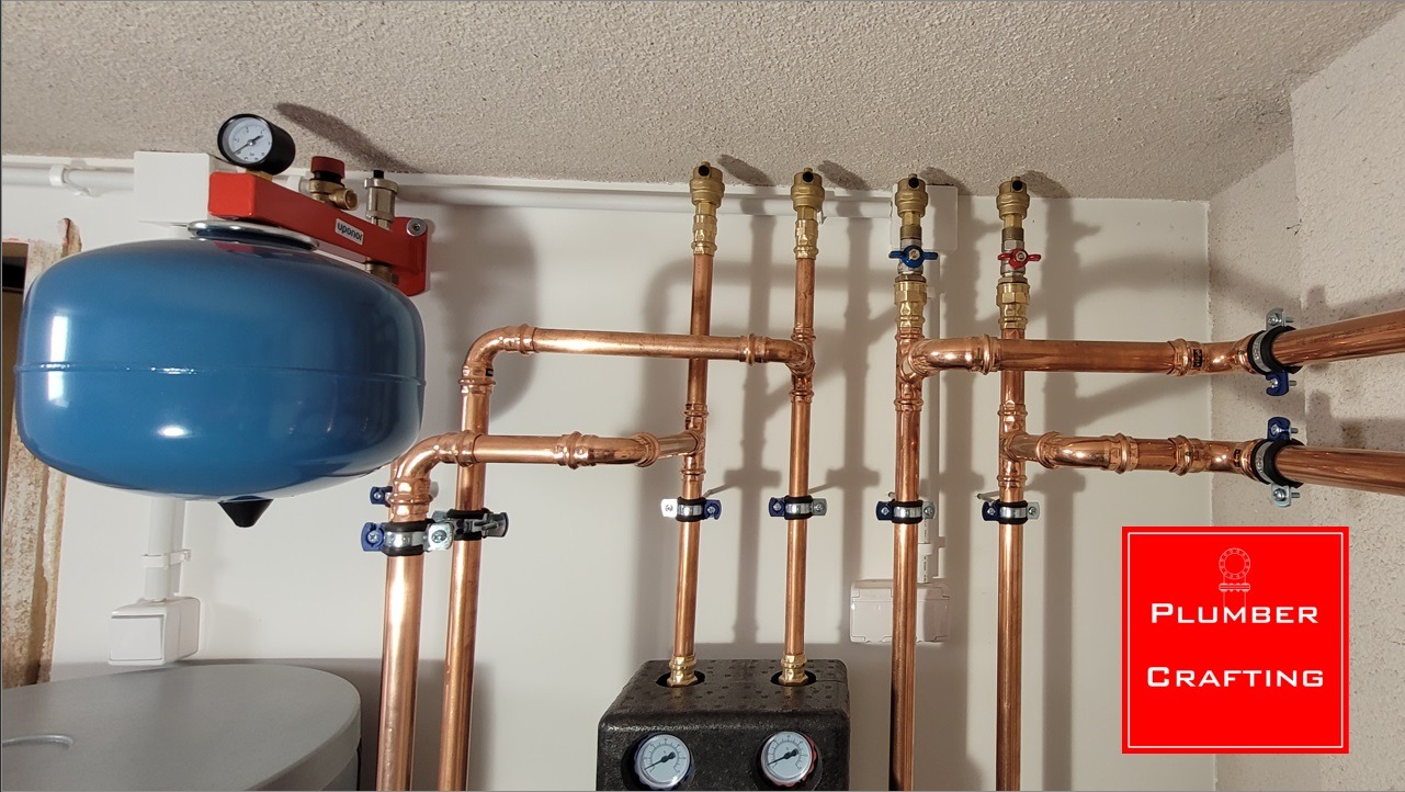 Nowoczesna instalacja grzewcza z miedzianymi rurami, zbiornikiem wyrównawczym i kotłem, połączona na ścianie w jasnym pomieszczeniu.