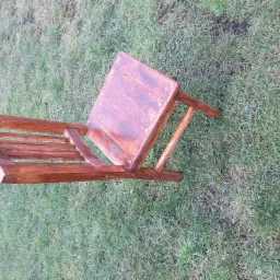 Drewniane krzesło ogrodowe, pomalowane bejcą na brązowo, leży na trawie. Widok z góry, ukazujący konstrukcję siedziska i oparcia.