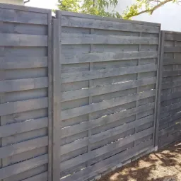 Nowoczesne, poziome ogrodzenie z desek pomalowanych na szaro, z widocznym drzewem i fragmentem trawnika.