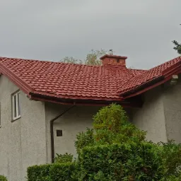 Czerwona dachówka na domu z kominem z cegły i ozdobną chorągiewką, widok z poziomu ogrodu.