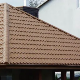 Brązowe pokrycie dachowe z blachy na budynku z białymi ścianami i ciemnym kominem.