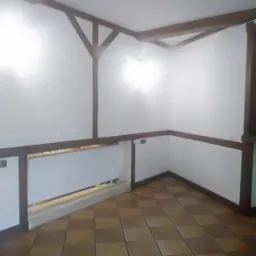 Wnętrze pokoju z brązowymi belkami stropowymi, białe ściany, terakota na podłodze i biała barierka.