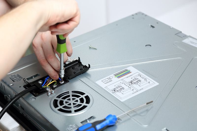 Podłączenie przewodów do płyty indukcyjnej od spodu, widoczne schematy połączeń i narzędzia.