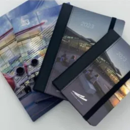 Stos kalendarzy książkowych i broszur na rok 2023 z motywem nowoczesnej architektury lotniskowej.