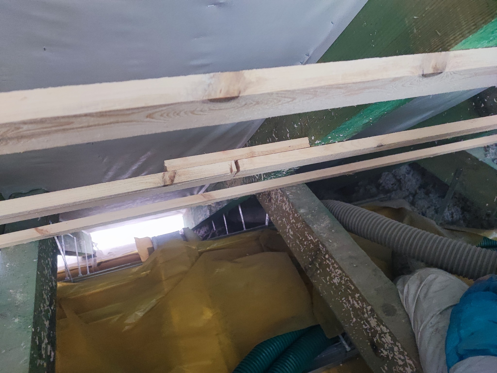 Szkielet drewniany poddasza w trakcie prac, widoczna folia paroizolacyjna, rura wentylacyjna i fragment ocieplenia z waty mineralnej.