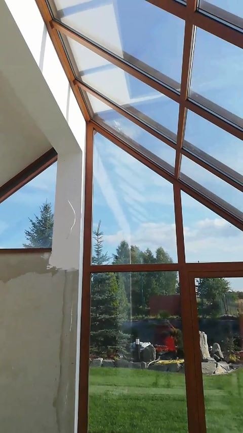 Wnętrze z drewnianą konstrukcją dachu i dużymi oknami z widokiem na ogród, ściana w stanie surowym.