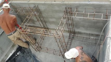 Zbrojenie w szalunku betonowym podczas budowy. Widoczne stalowe pręty tworzące konstrukcję wzmacniającą, przygotowane do zalania betonem. Dwóch pracowników w roboczych ubraniach i czapkach ustawia...