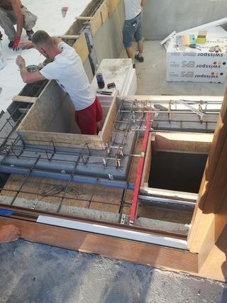 Prace budowlane na balkonie: zbrojenie, szalunek i poziomica w trakcie montażu. Widoczni pracownicy w tle.