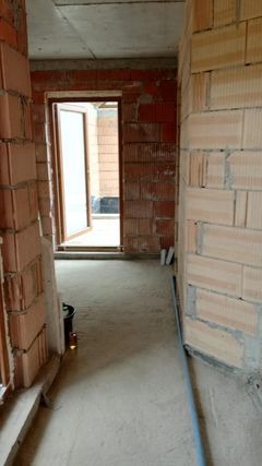 Surowy stan wnętrza budynku w trakcie budowy: ściany z cegły ceramicznej Porotherm, surowy betonowy sufit, widoczne otwory okienne i drzwiowe, podłoże wylewka betonowa, przygotowane do dalszych...