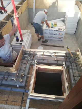 Dwóch pracowników podczas montażu szalunku i zbrojenia pod wylewkę betonową, widoczne płyty styropianowe Swissopor i narzędzia.