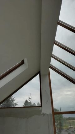 Poddasze z oknami dachowymi o nietypowym kształcie, ściany w trakcie wykończenia, widoczne ślady po gładzi szpachlowej.