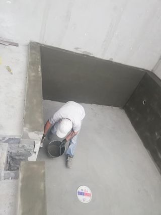 Pracownik w białej koszulce i czapce nakłada zaprawę na ścianę i sufit w pomieszczeniu, widok z góry na etap wykończenia wnętrza.