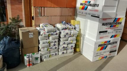 Materiały budowlane: cegły, styropian Austrotherm, worki z zaprawą klejową i piana montażowa zgromadzone przed rozpoczęciem prac budowlanych.