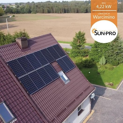 Widok z góry na dom z brązowym dachem, na którym zamontowano panele słoneczne; widoczny komin, okno dachowe i logo firmy SUN-PRO z informacją o mocy 4,22kW i lokalizacji Warcimino.