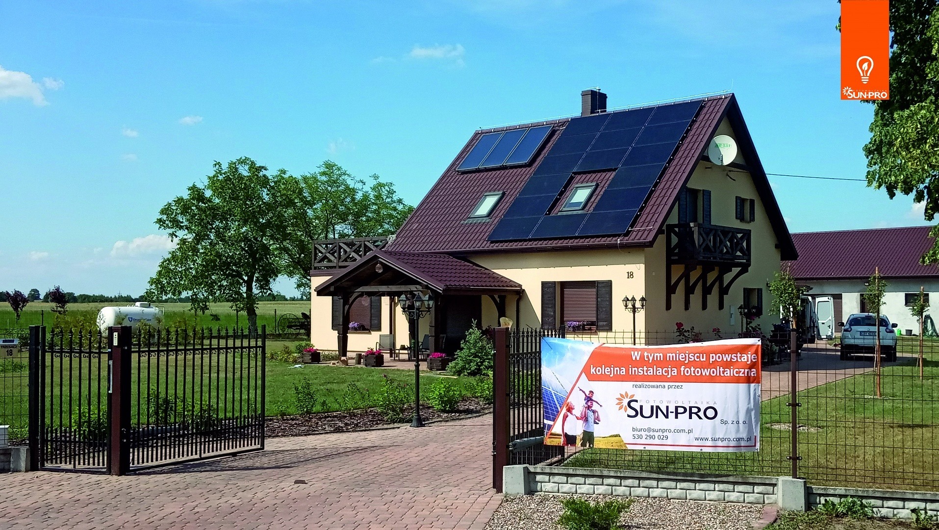 Dom jednorodzinny z zainstalowanymi panelami słonecznymi na dachu, widoczny baner reklamowy firmy instalującej system.