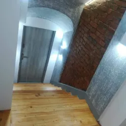 Klatka schodowa z drewnianymi schodami, ceglaną ścianą i łukowym sufitem z oświetleniem LED.