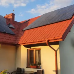 Dom jednorodzinny z panelami słonecznymi na czerwonym dachu, widok z poziomu ogrodu w słoneczny dzień.