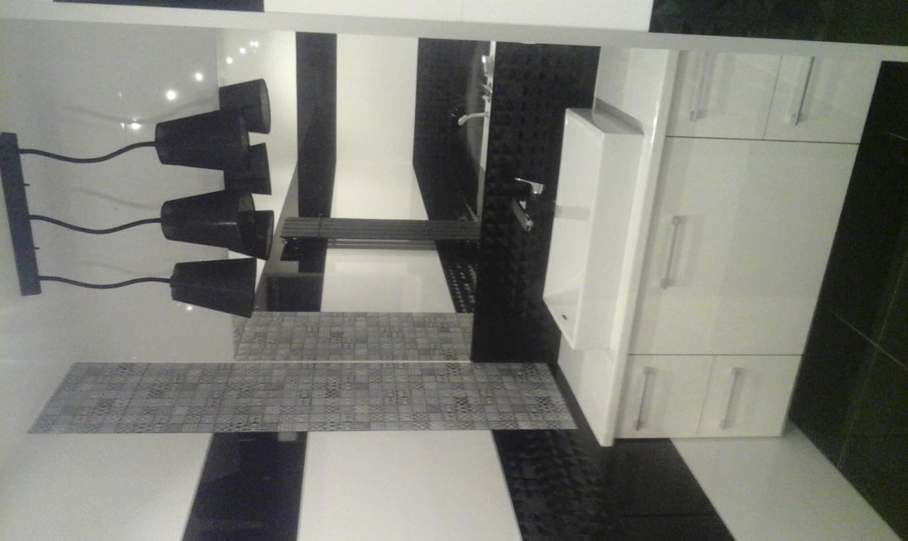 Nowoczesna łazienka w czarno-białej kolorystyce z wiszącą szafką umywalkową, mozaiką ścienną i designerską lampą z czarnymi abażurami.