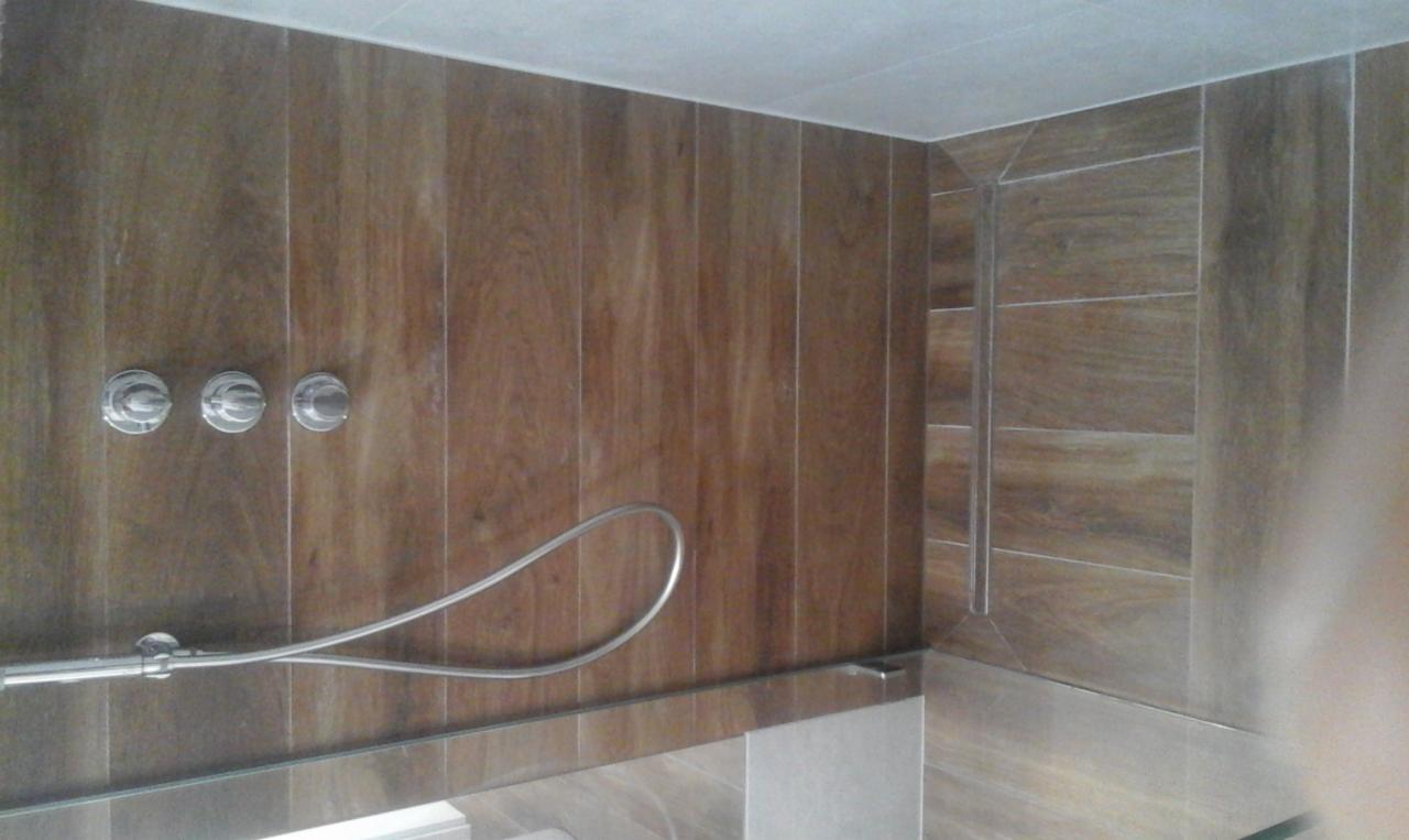 Wykończona kabina prysznicowa z drewnopodobnymi płytkami, chromowaną armaturą i szklanym panelem.