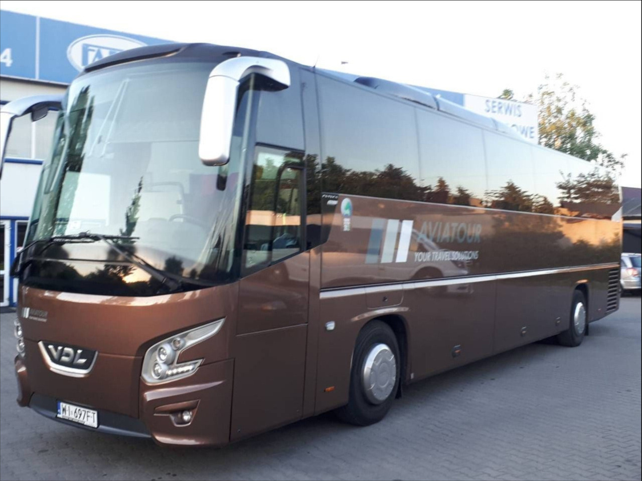 Brązowy autokar firmy Aviatour z numerem rejestracyjnym W1 697FT, zaparkowany na zewnątrz, widoczny z boku.