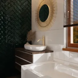 Nowoczesna łazienka z zielonymi płytkami ułożonymi w jodełkę, okrągłym lustrem w złotej ramie, białą umywalką na drewnianej szafce i oknem z widokiem na jesienne drzewa.