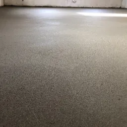 Świeżo wylana, gładka posadzka jastrychowa w surowym wnętrzu, widoczne ślady po obróbce, jasne światło padające z góry.