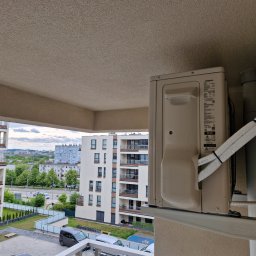 INSTALMATE Mateusz Ząbek - Klimatyzator zamontowany na balkonie nowoczesnego apartamentowca, widok na miasto w tle. Estetyczny montaż z widocznymi przewodami i elementami mocującymi.
