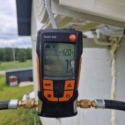 INSTALMATE Mateusz Ząbek - Pomiar temperatury klimatyzacji zewnętrznym miernikiem Testo 552, podłączonym do instalacji. Widoczne węże i ekran urządzenia z odczytem.