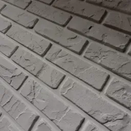 Ściana z dekoracyjnej cegły w odcieniach szarości, ułożona pod kątem, z widoczną fakturą i nierównościami powierzchni.