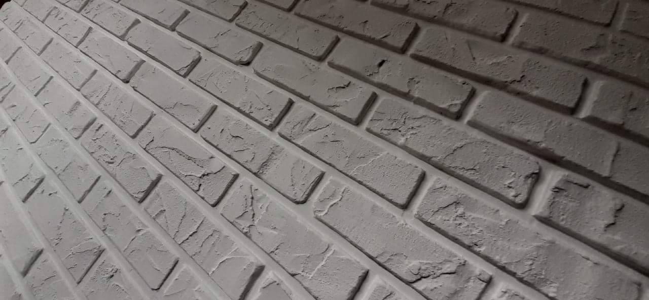 Ściana z dekoracyjnej cegły w odcieniach szarości, ułożona pod kątem, z widoczną fakturą i nierównościami powierzchni.