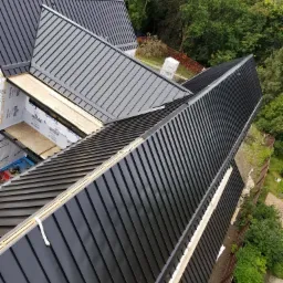 Montaż paneli dachowych z blachy na nowym budynku, widok z góry, widoczne fragmenty izolacji i konstrukcji dachu przed ostatecznym wykończeniem.