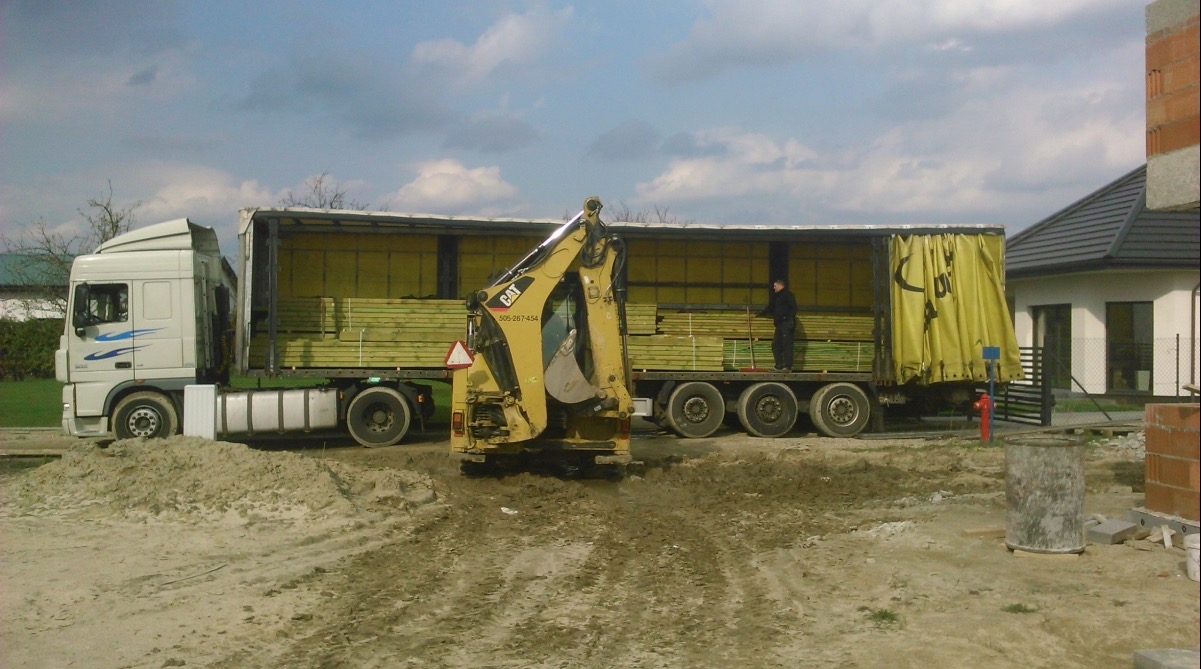 Załadunek impregnowanej tarcicy budowlanej na ciężarówkę za pomocą koparki CAT na placu budowy.
