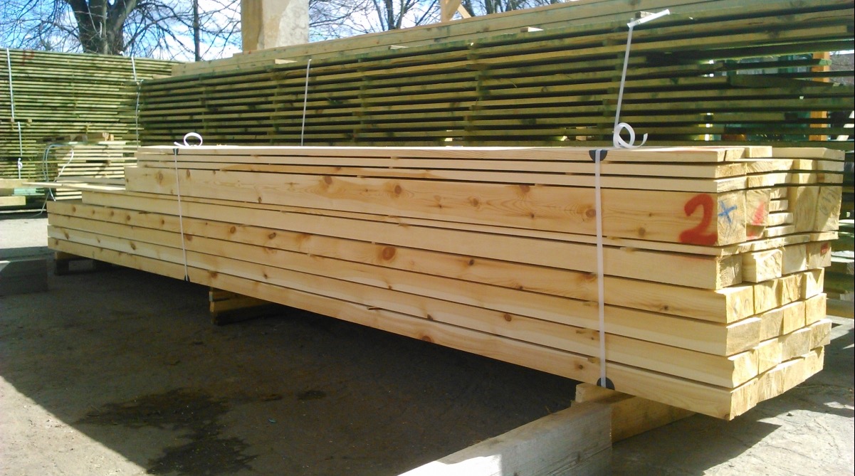 Stosy świeżo przetartej tarcicy sosnowej, składowane na drewnianych podkładach, z widocznym oznaczeniem '2' na jednym z pakietów i zapakowane taśmą.