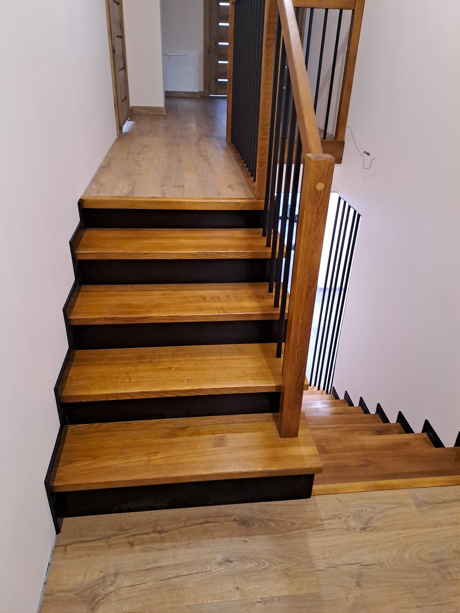 Nowoczesne schody z drewnianymi stopniami i czarną metalową balustradą w domu w Lniano, widok z góry na dół.