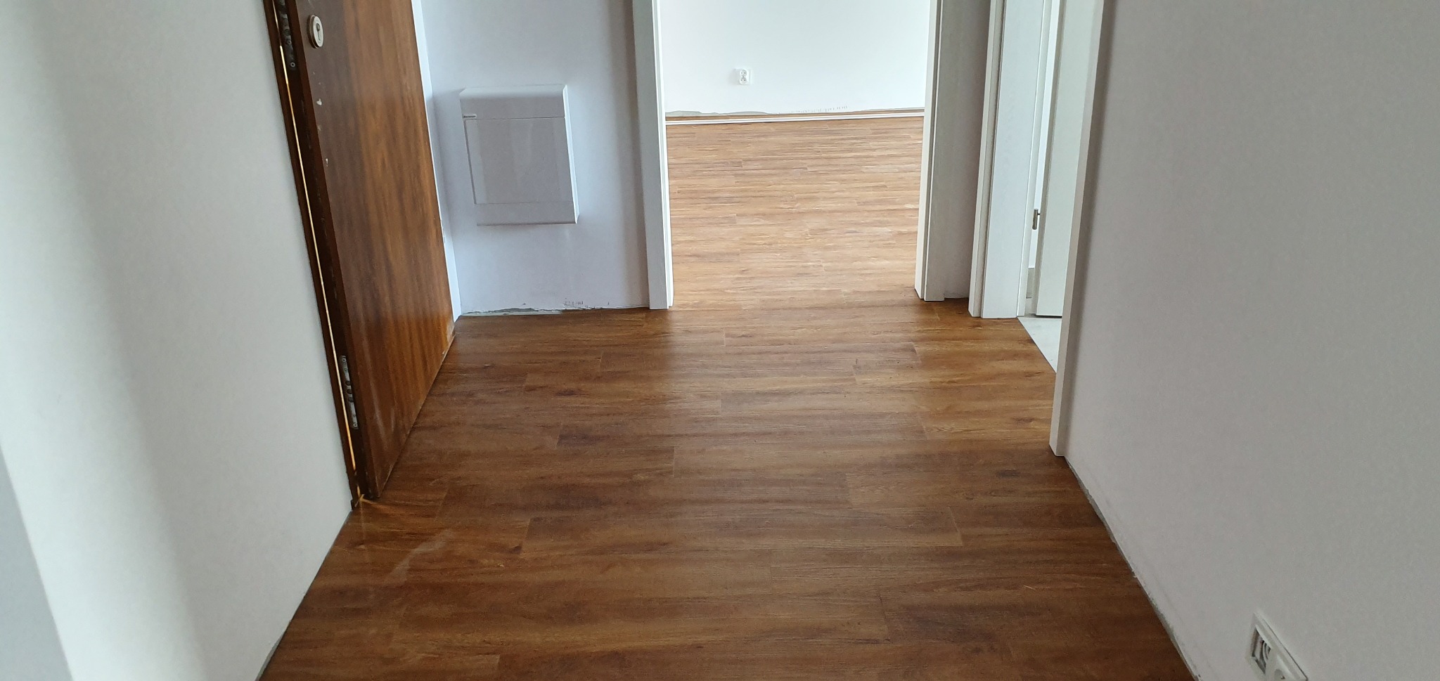 Korytarz z nową, brązową wykładziną imitującą drewno, widok w głąb mieszkania.