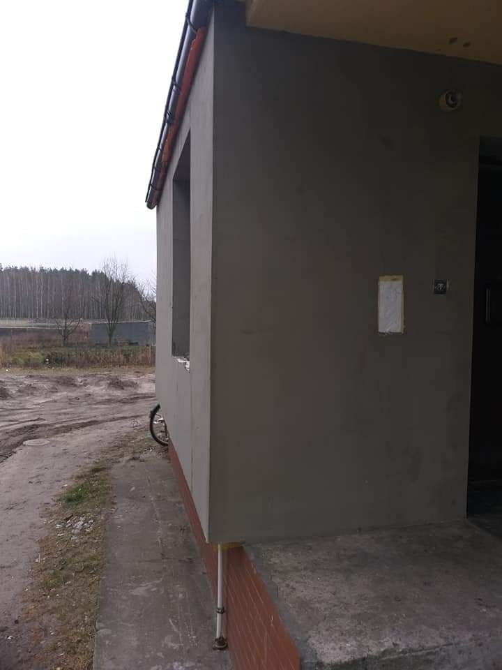 Budynek po nałożeniu tynku w Świeciu, widoczne okno bez ramy, fragment dachu z rynną i ceglana podmurówka. Na ścianie przyklejona kartka.