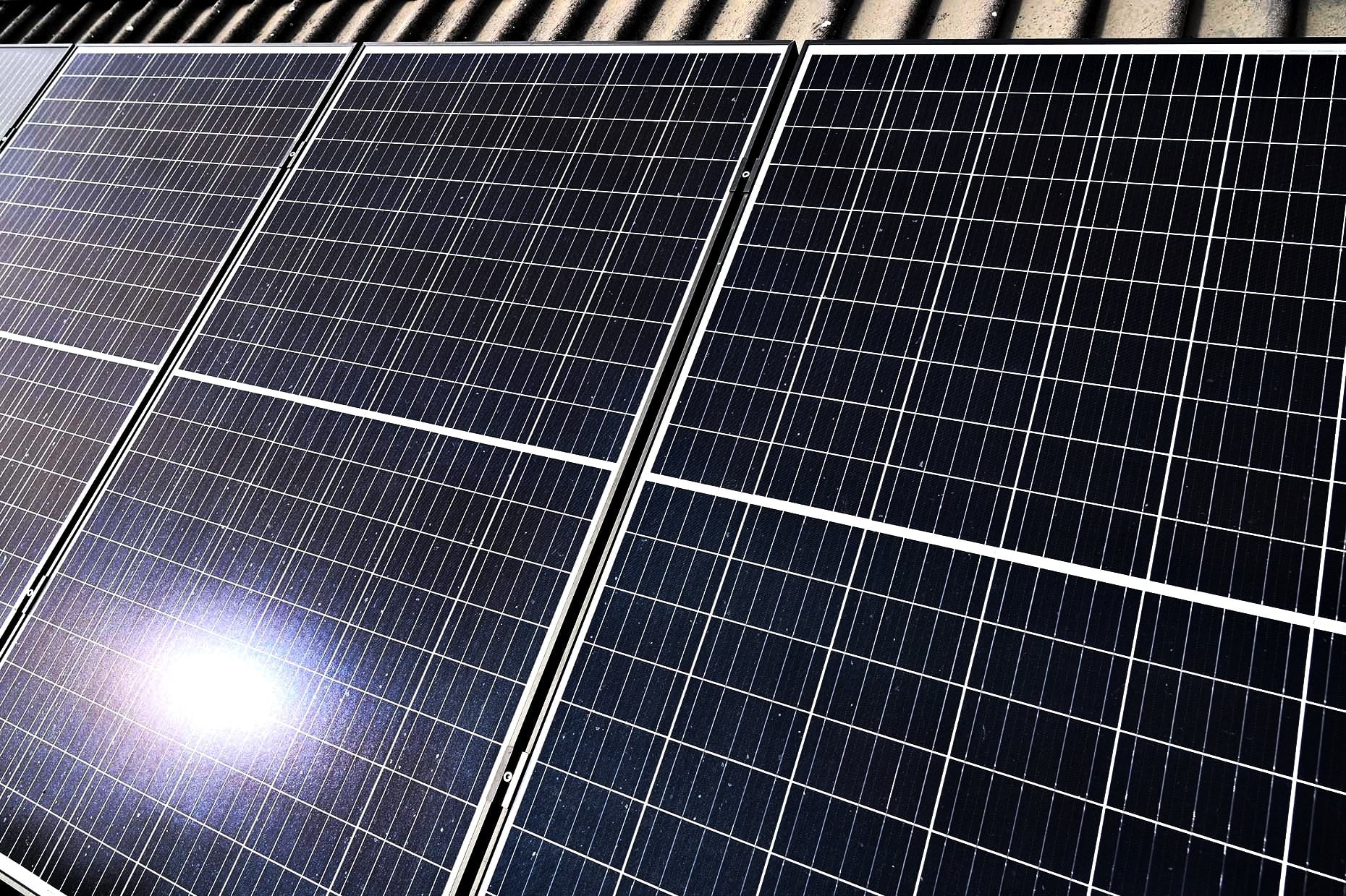 Rząd paneli słonecznych na dachu, z odbiciem słońca na jednym z paneli, ukazujący modułową konstrukcję i czyste linie krzemowych ogniw.