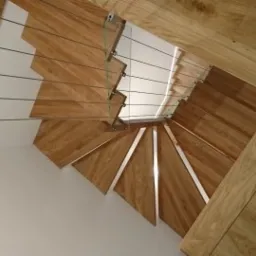 Spiralne stopnie z jasnego drewna, zabezpieczone stalowymi linkami, widoczne z góry, z dopasowaną drewnianą podłogą.
