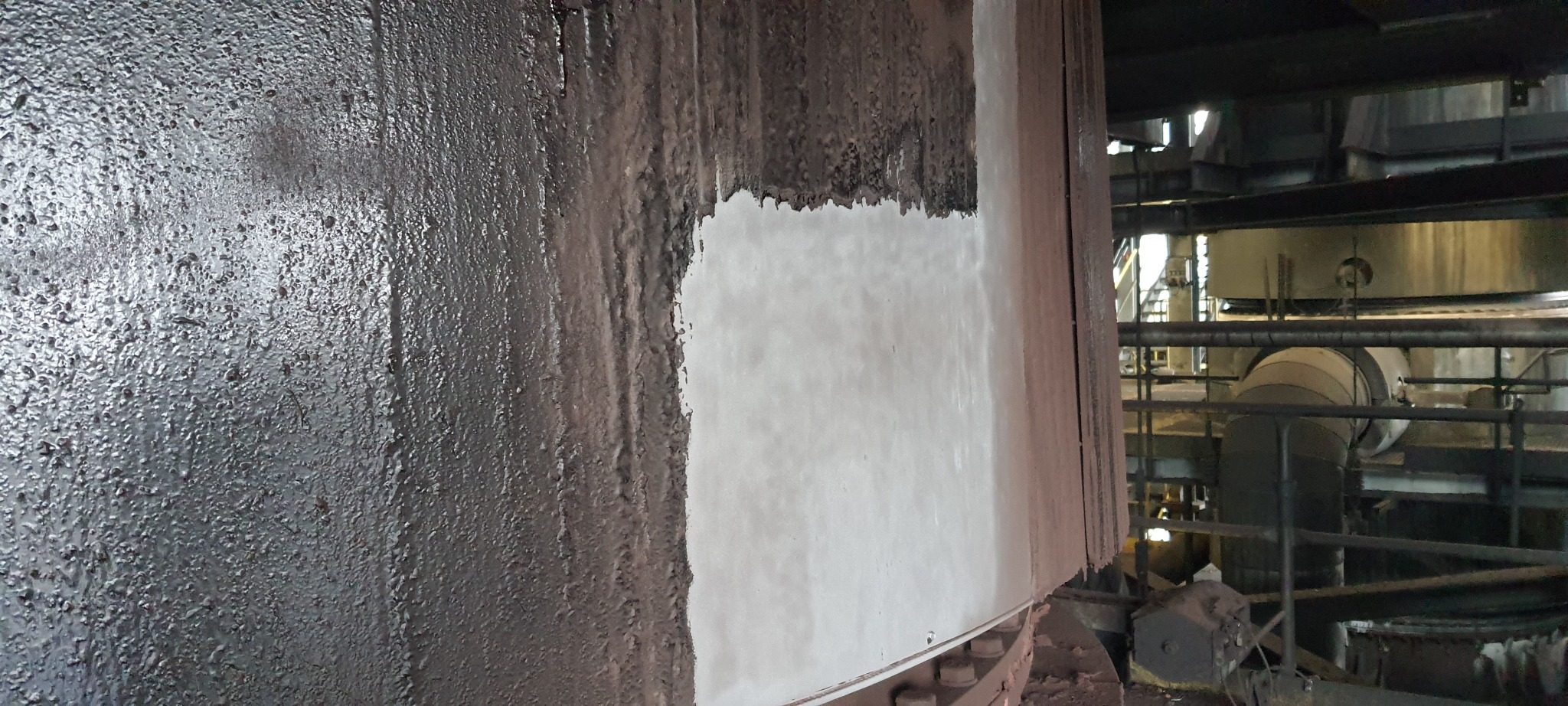 Metalowa konstrukcja, częściowo oczyszczona, z widocznymi śladami rdzy i resztek starej powłoki, z fragmentem czystej, jasnej powierzchni po obróbce.