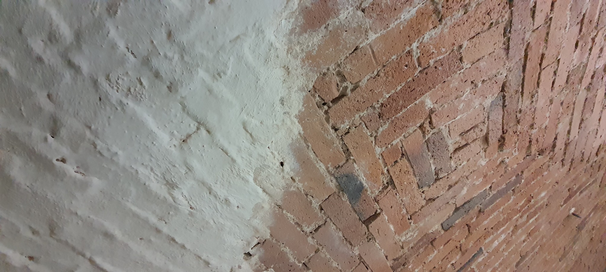 Fragment ceglanej ściany z nałożoną warstwą białej farby, ukazujący kontrast między surową cegłą a pomalowaną powierzchnią.