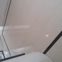 Jasne, kwadratowe płytki podłogowe z czarnym, marmurkowym pasem dekoracyjnym; widoczne narzędzia i szmatki do czyszczenia w rogu.