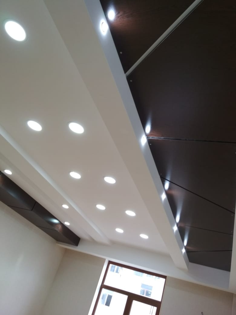Biały sufit podwieszany z wbudowanymi okrągłymi lampami LED, połączony z ciemnobrązowymi panelami na suficie, widok z dołu, okno w tle.