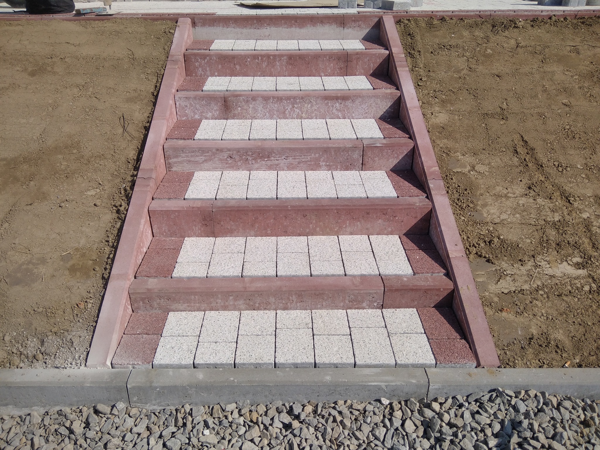 Schody zewnętrzne z czerwonej i szarej kostki brukowej, widok z góry, obok ziemia i kamień ozdobny.