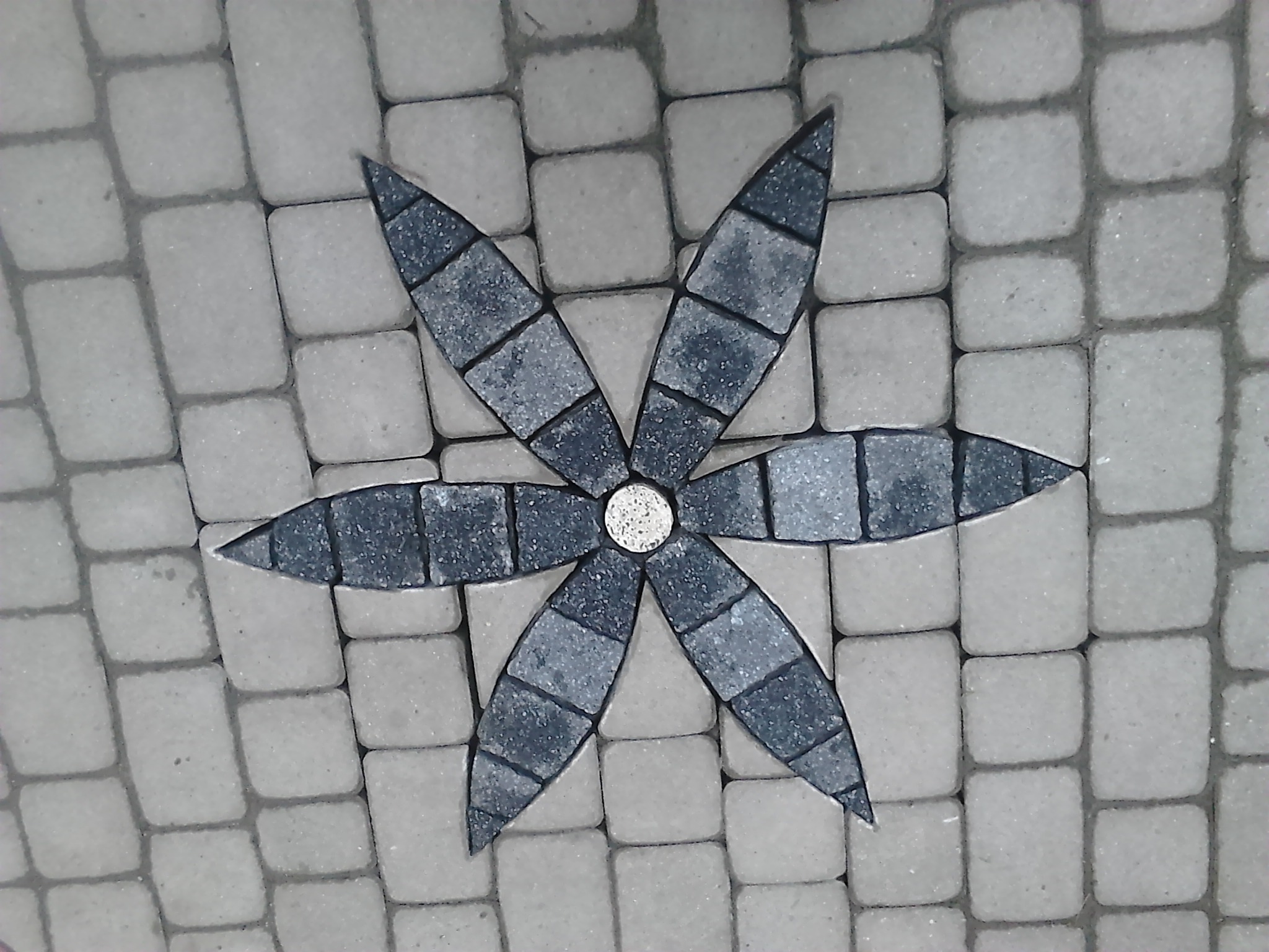 Dekoracyjny wzór kwiatowy ułożony z ciemnoszarych i jasnoszarych kostek brukowych, widok z góry.