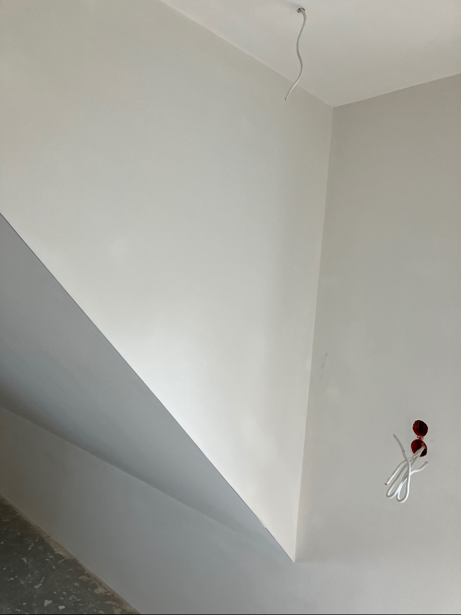 Świeżo pomalowane na biało ściany i szary sufit w rogu pomieszczenia z wystającymi przewodami elektrycznymi z sufitu i ściany.