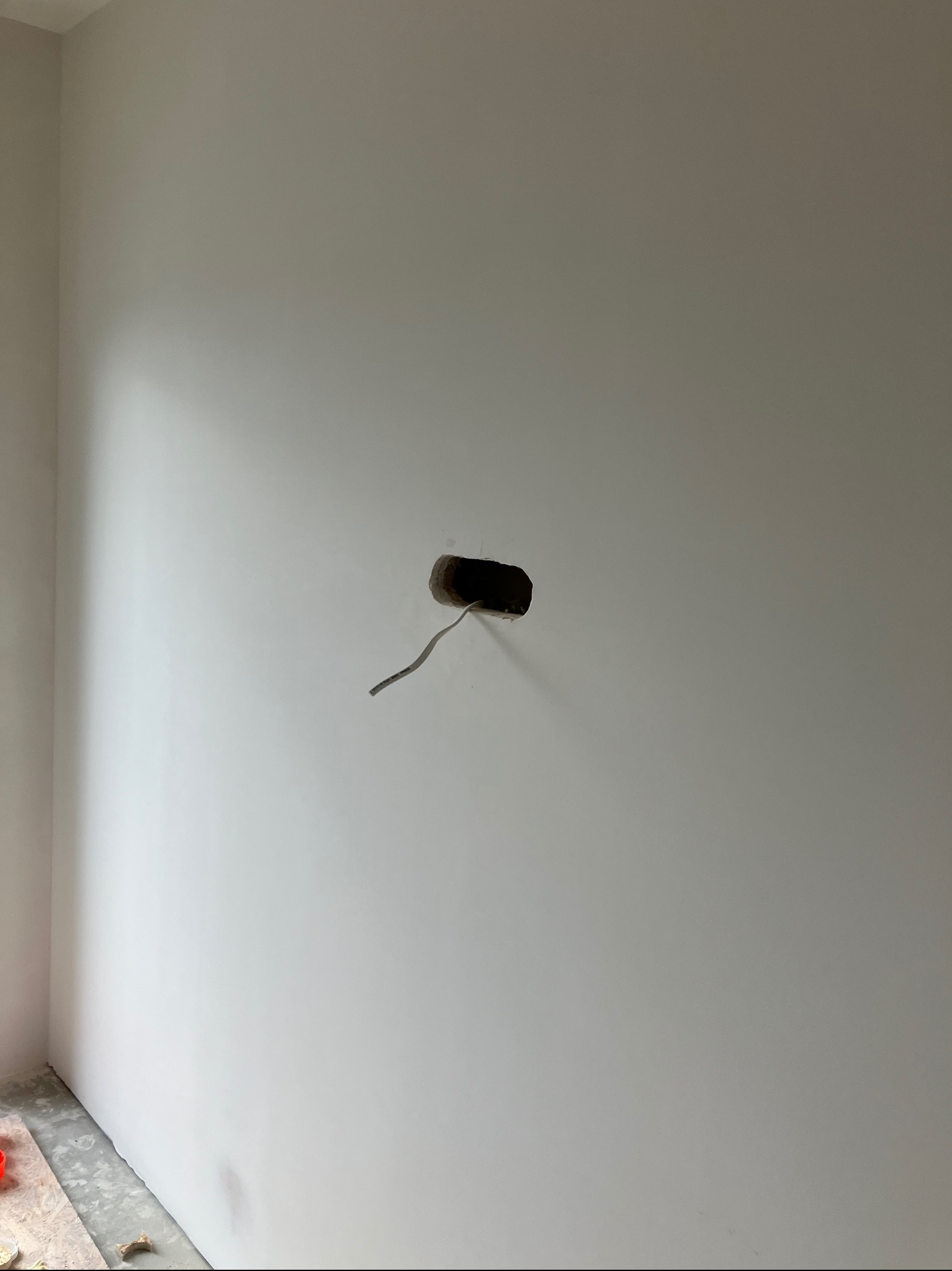 Świeżo pomalowana, gładka, biała ściana z otworem na gniazdko elektryczne i wystającym kablem, przygotowana do montażu osprzętu.