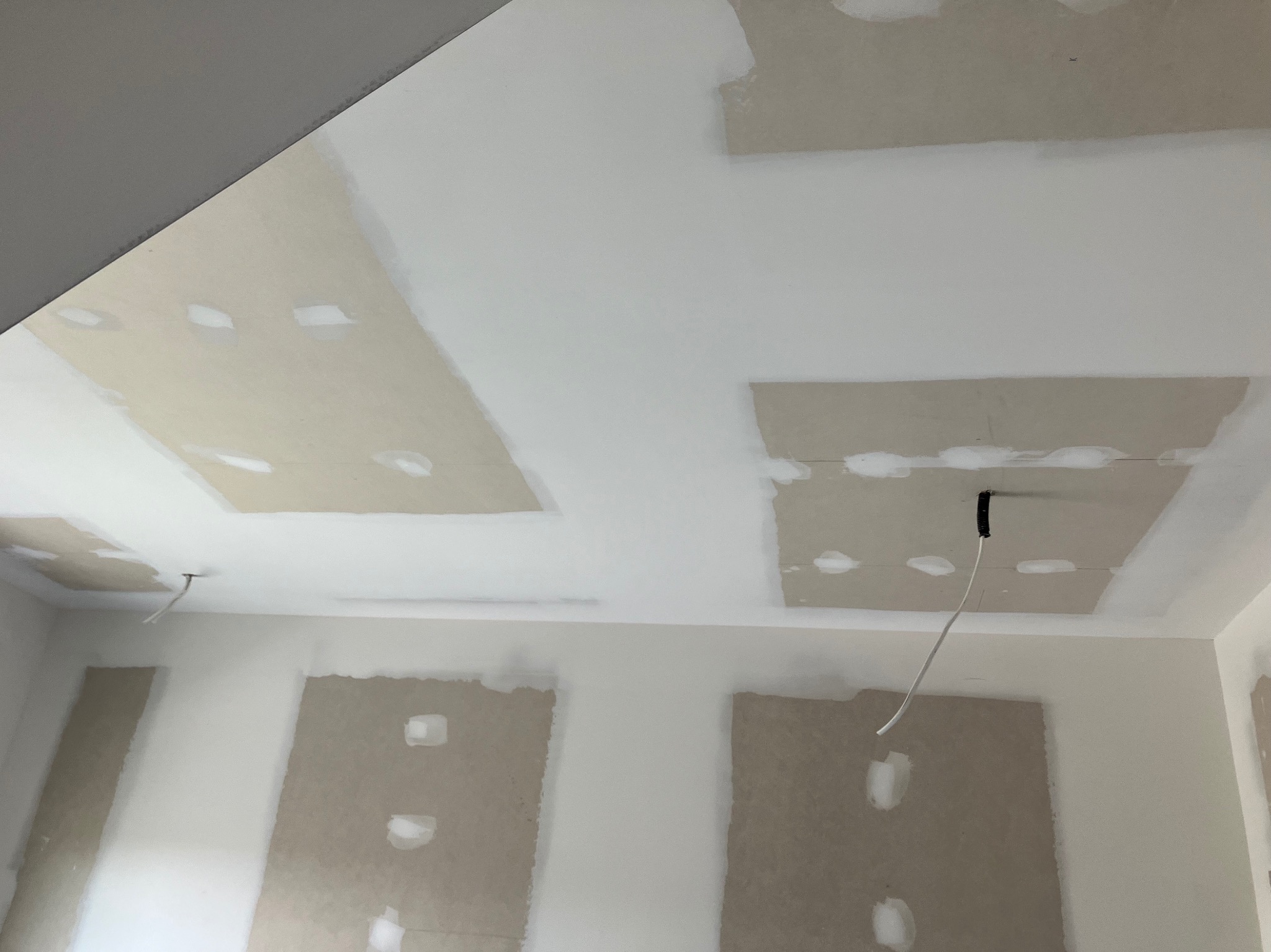 Ściana i sufit w trakcie przygotowania do malowania: płyty gipsowo-kartonowe częściowo pokryte gładzią, widoczne przewody elektryczne wystające z sufitu.
